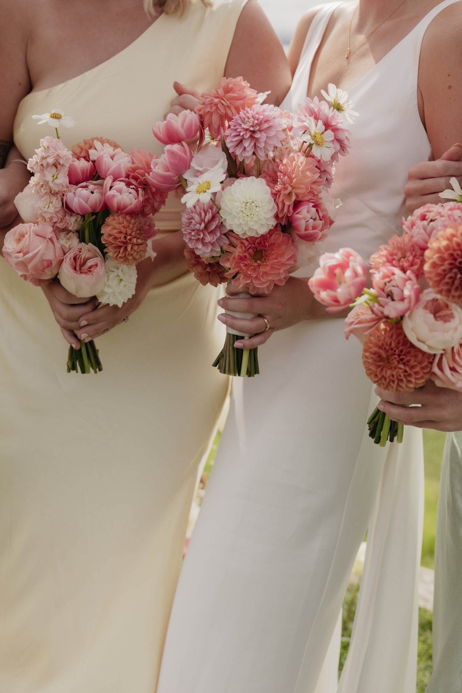 Two women holding pink and white flower bouquets, one in a light-colored dress and the other in a white dress.