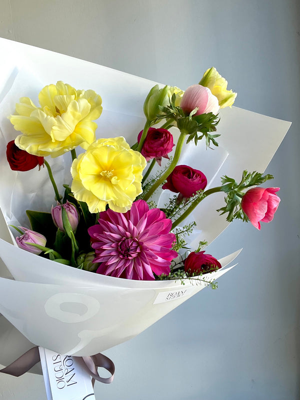 Bouquet of spring flowers wrapped in white paper with a gray background