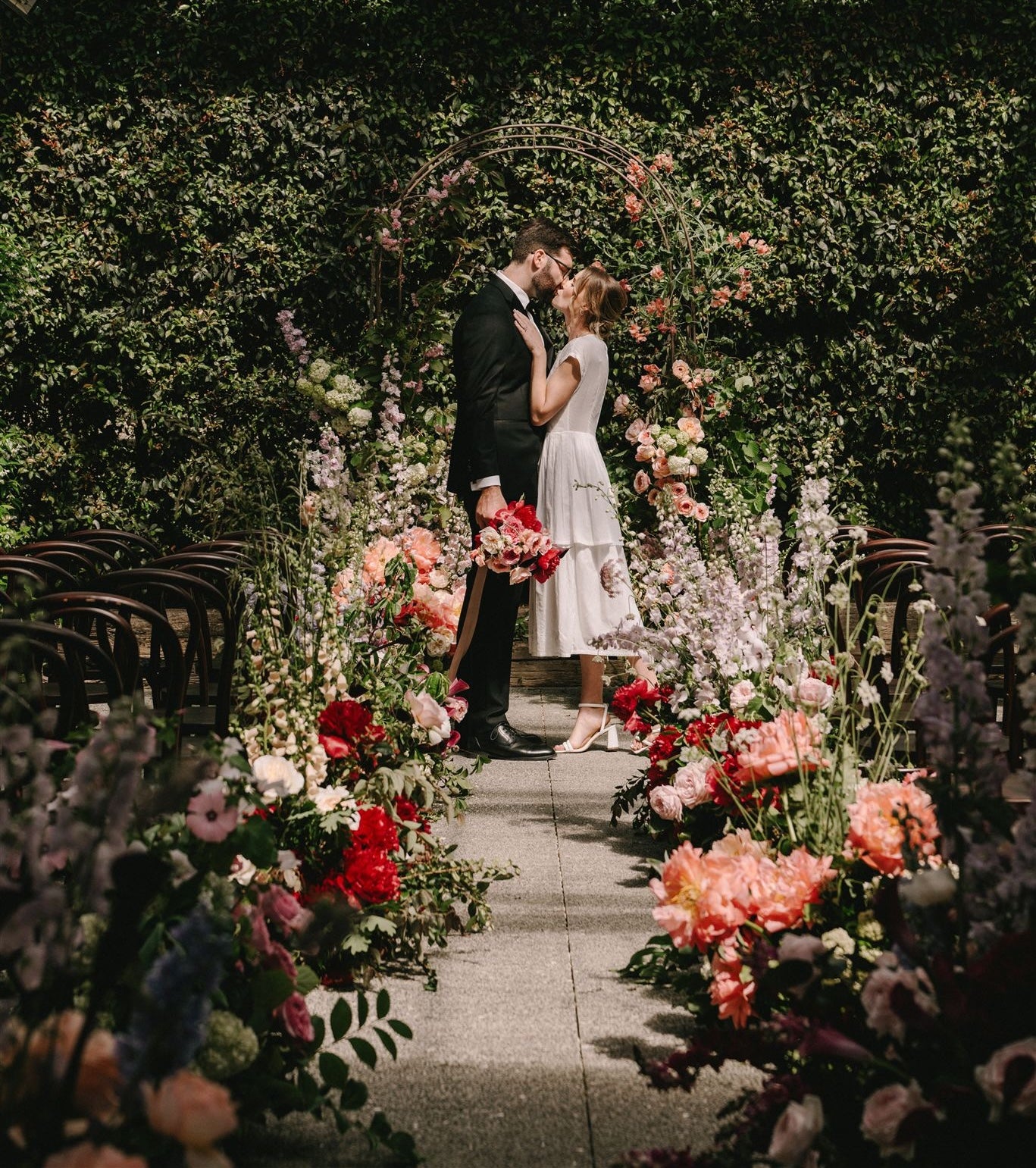 Couple kissing under a floral archway in a garden setting