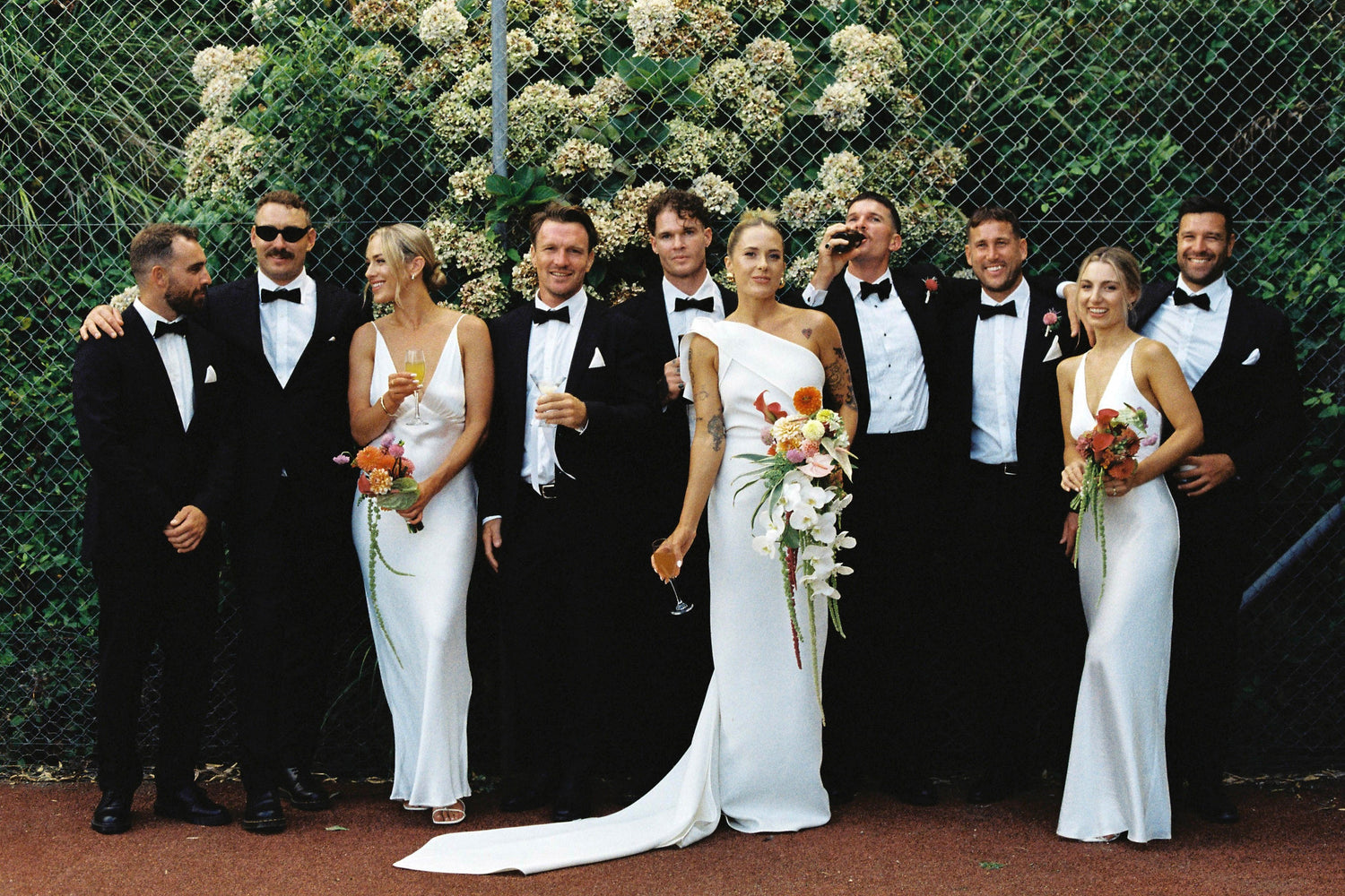 Group of people in formal attire standing outdoors with floral arrangements.