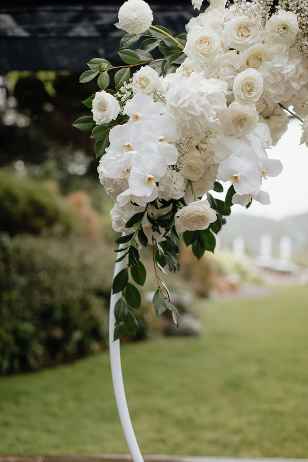 Floral archway with white flowers and green leaves on a blurred outdoor background