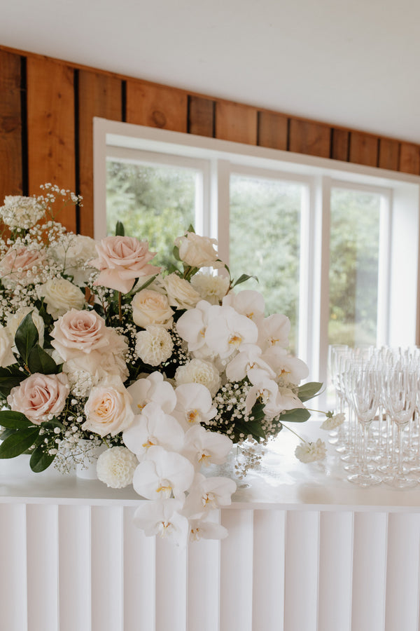 Floral arrangement on a bar with a wooden wall and window in the background
