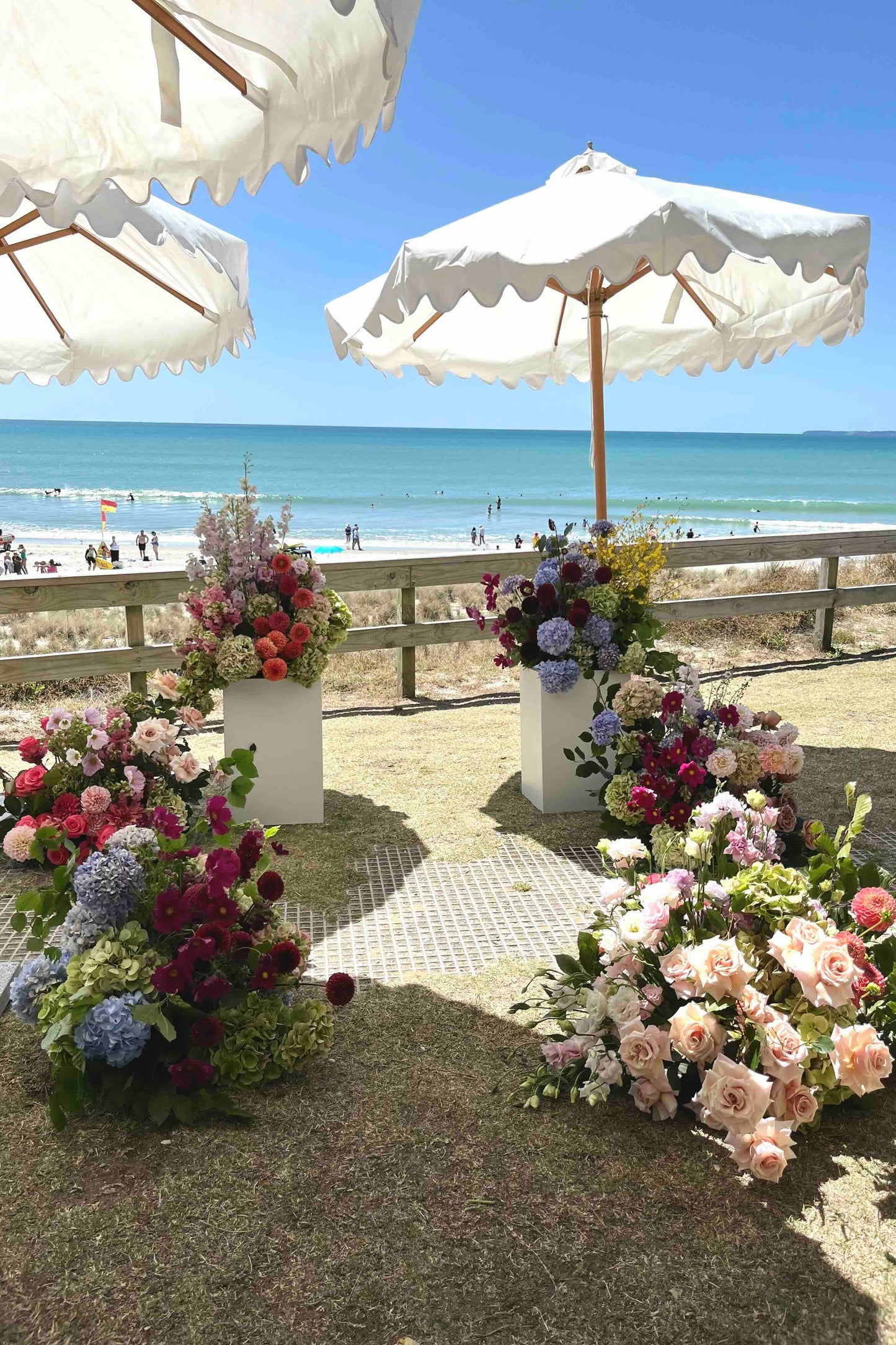 Decorative floral arrangements with white umbrellas on a sandy beach.