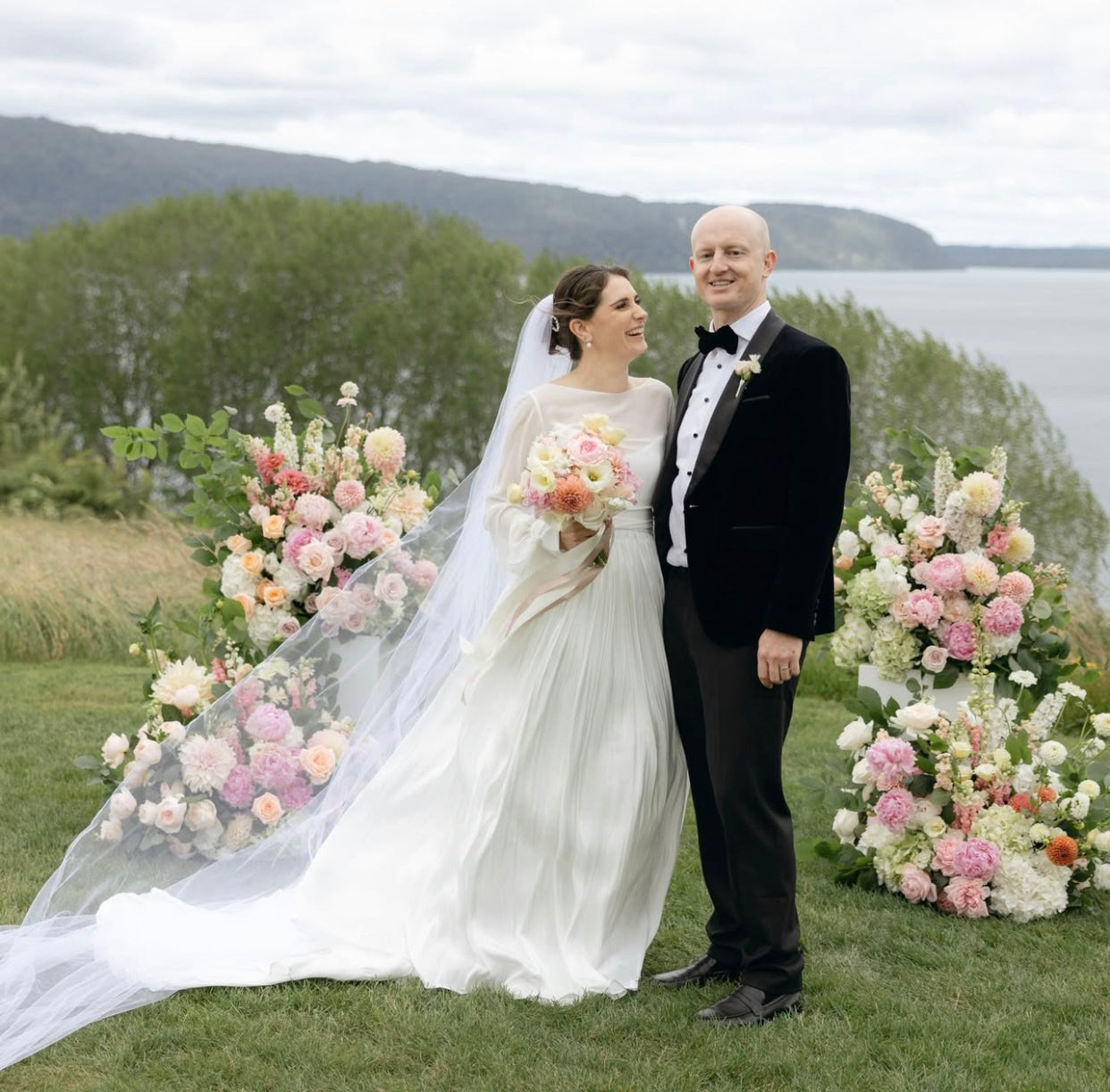 Wedding couple standing in front of floral plinths with a scenic background.