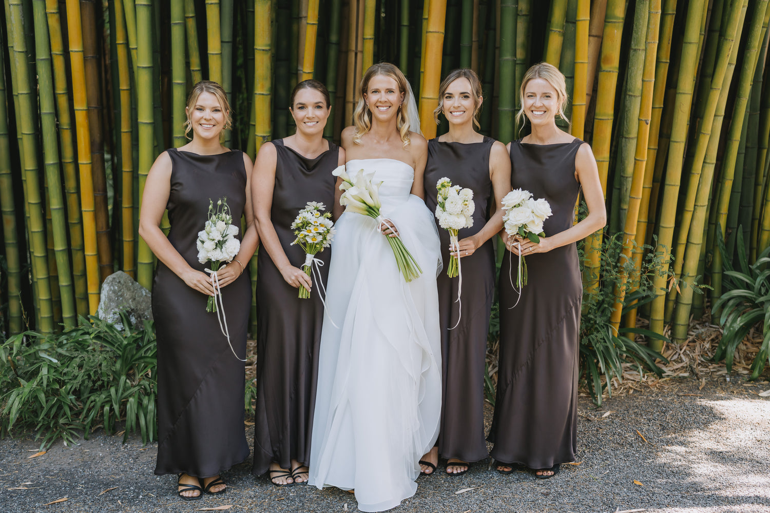Bride and bridesmaids in front of a bamboo wall with bridal bouquet flowers