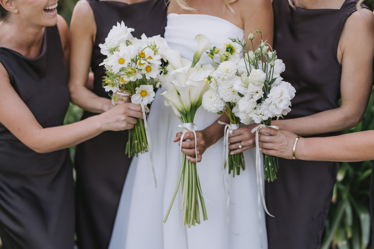 Bride with white dress holding flower bouquets, surrounded by three women in brown dresses.