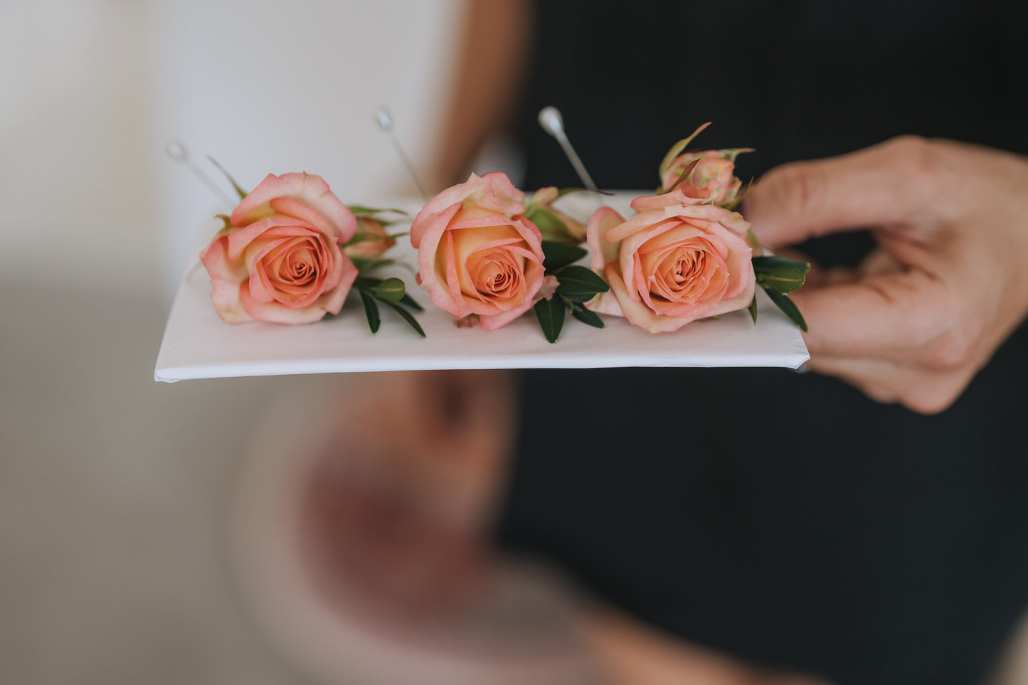 Person holding three buttonholes of pink roses on a white card
