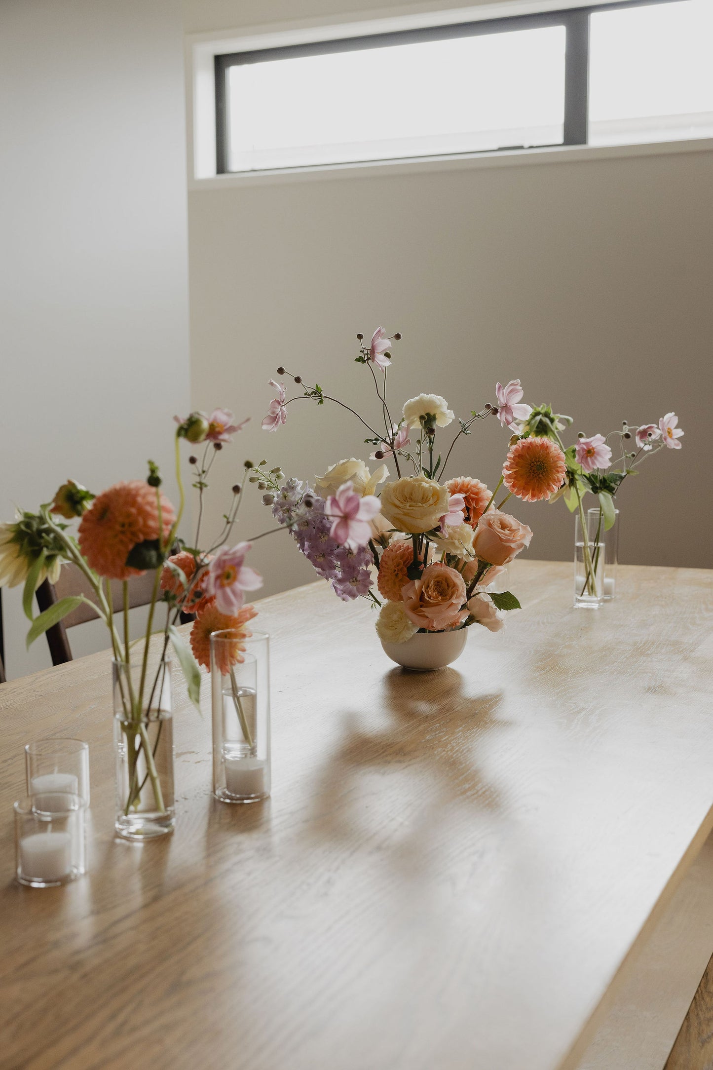 Floral arrangements in vases on a wooden table with a window in the background