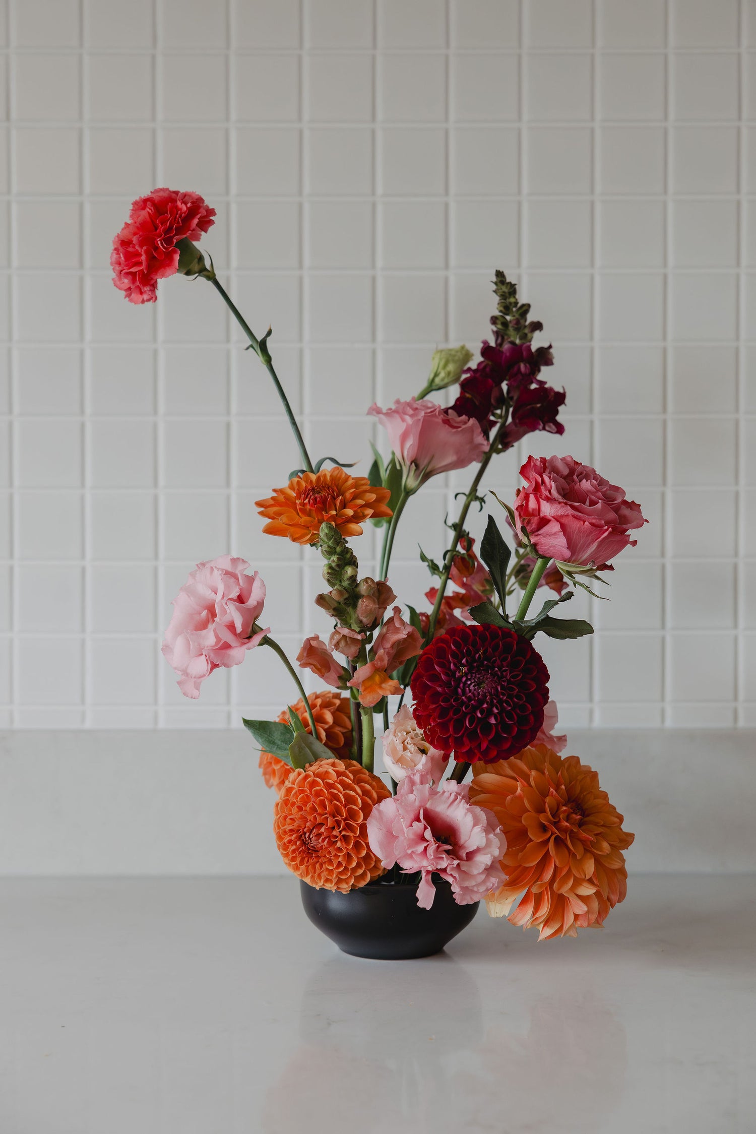 Bright floral arrangement in a black vase against a white tiled wall.