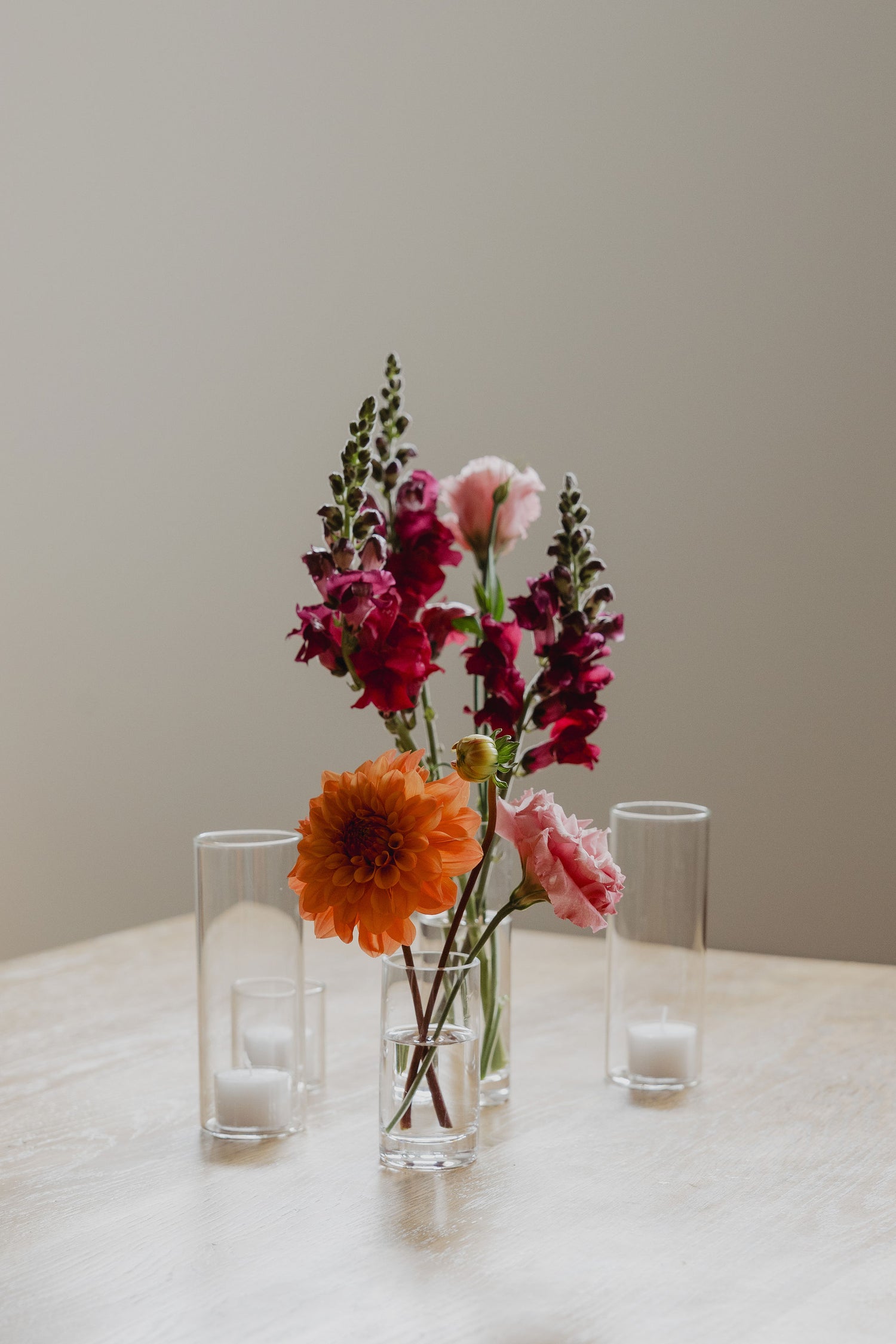 bud vases with flowers and tealight candles on a table against a plain wall