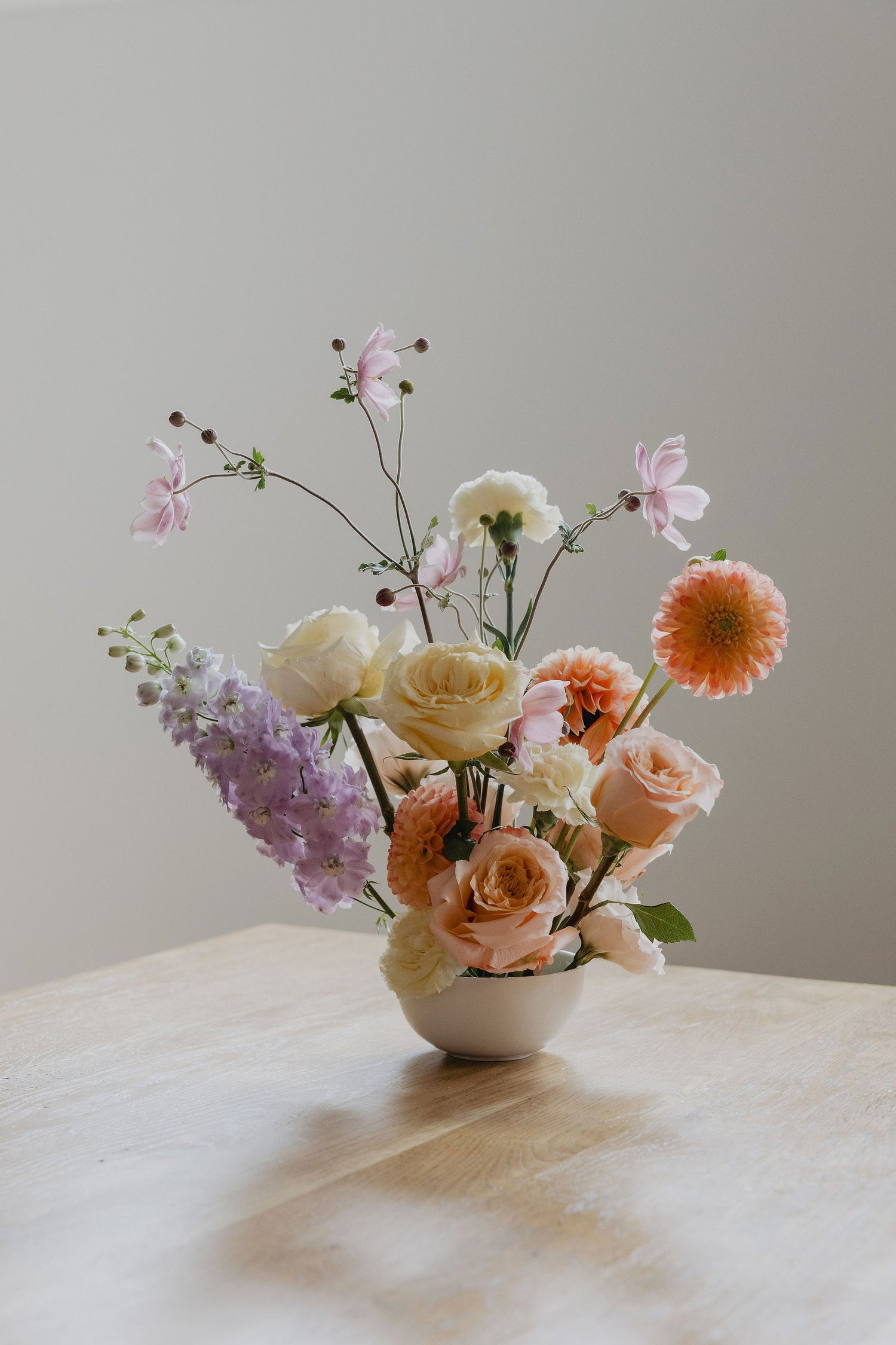 Pastel flowers in a white bowl on a wooden surface with a neutral background