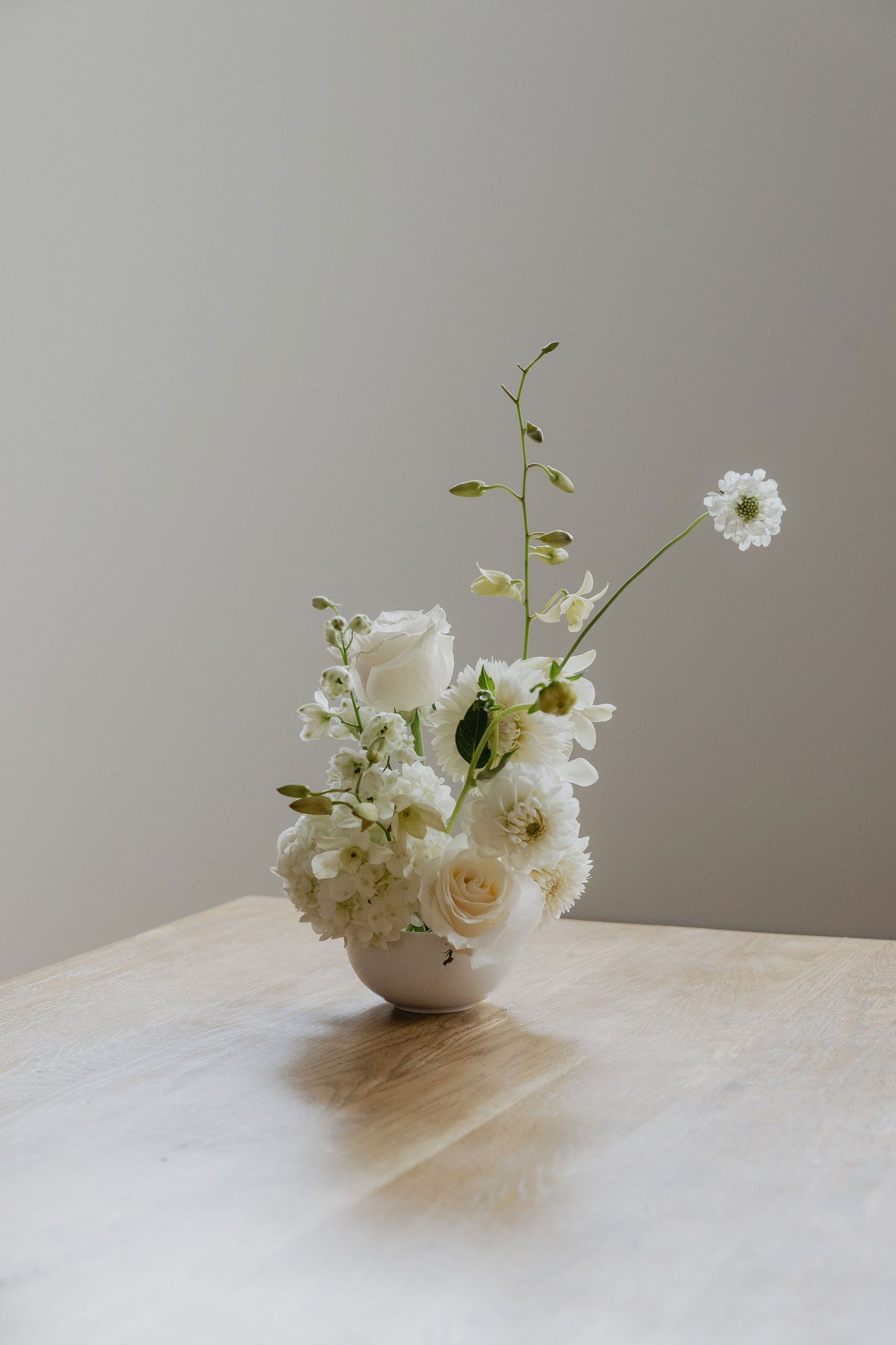 Small arrangement of white flowers in a white bowl on a wood surface with a neutral background