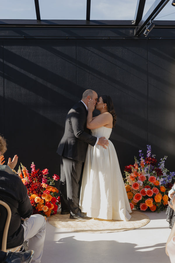 Couple sharing a kiss at a wedding ceremony with colourful flowers in the background.