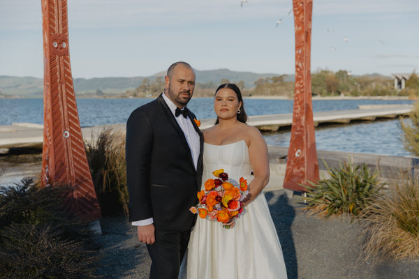Couple standing by a waterfront with a scenic background and colourful spring wedding bouquet