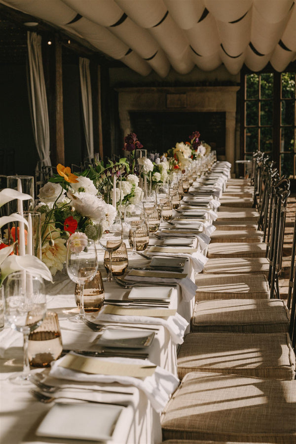 Long table set for a formal event with floral arrangements and white tablecloths.